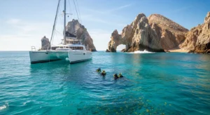 A luxury catamaran anchored in clear Los Cabos waters with snorkelers swimming nearby.