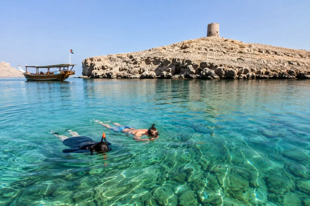Wooden dhow boat over turquoise Musandam snorkeling spots with diver and coral reef below