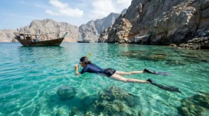 Boat with snorkeler above coral reef at Musandam snorkeling spots in clear blue mountain water sea