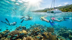 Snorkelers exploring a coral reef during an Ocho Rios snorkeling tour with a catamaran and Jamaica's coastline in the background.